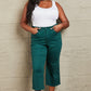 Woman wearing Hailey tummy control high waisted cropped wide leg Judy Blue Jeans in teal, standing against a textured wall.