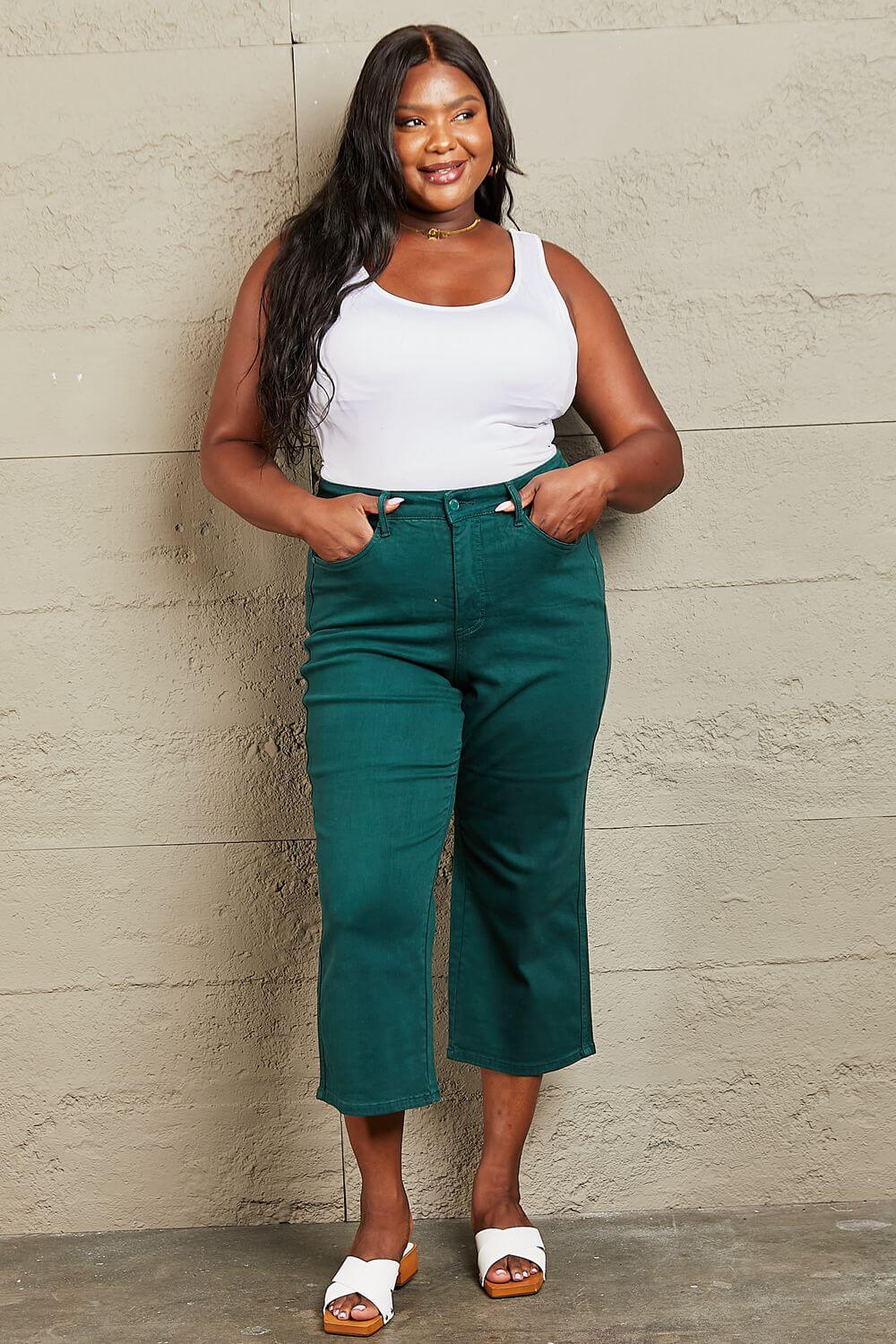 Woman wearing Hailey tummy control high waisted cropped wide leg Judy Blue Jeans in teal, standing against a textured wall.