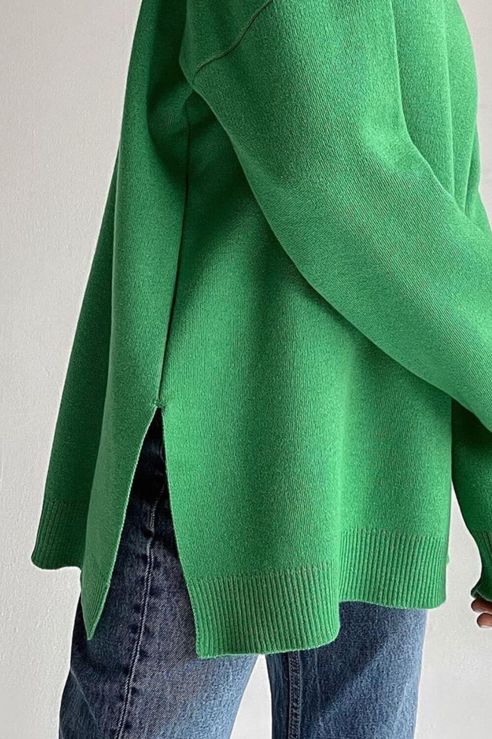 Cozy green side slit turtleneck sweater with dropped shoulders paired with jeans for a stylish and relaxed look.