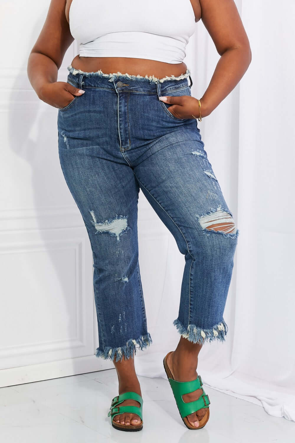 Woman modeling Undone Chic Straight Leg Jeans by Risen Jeans with distressed details, raw hem, and cropped length, paired with a white crop top.