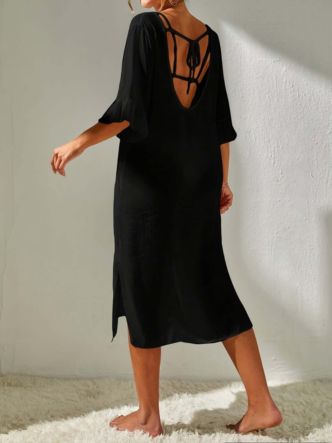 Woman wearing backless black slit V-neck flounce sleeve cover-up with tied details, made of sheer polyester material.