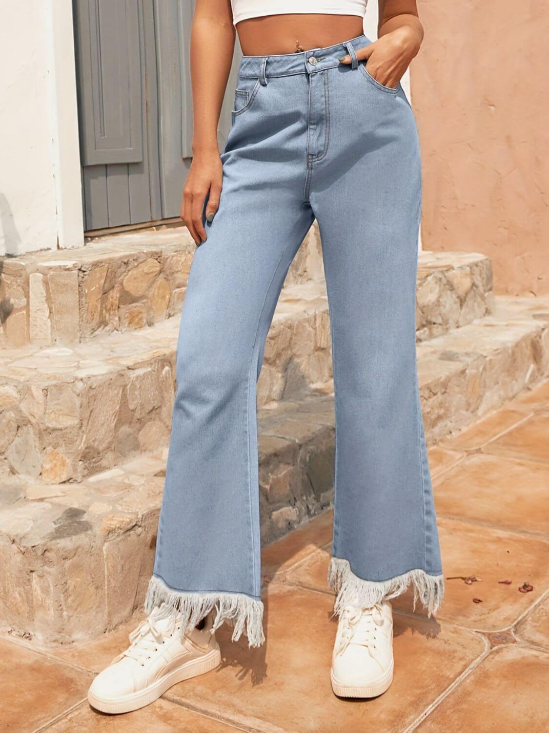 Woman wearing Bella Road light wash bootcut jeans with raw hem and pockets, styled with a trendy crop top and sneakers.