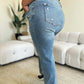 Person wearing high waist distressed straight jeans by Judy Blue, showing back pocket details and straight leg fit, in a stylish living room setting