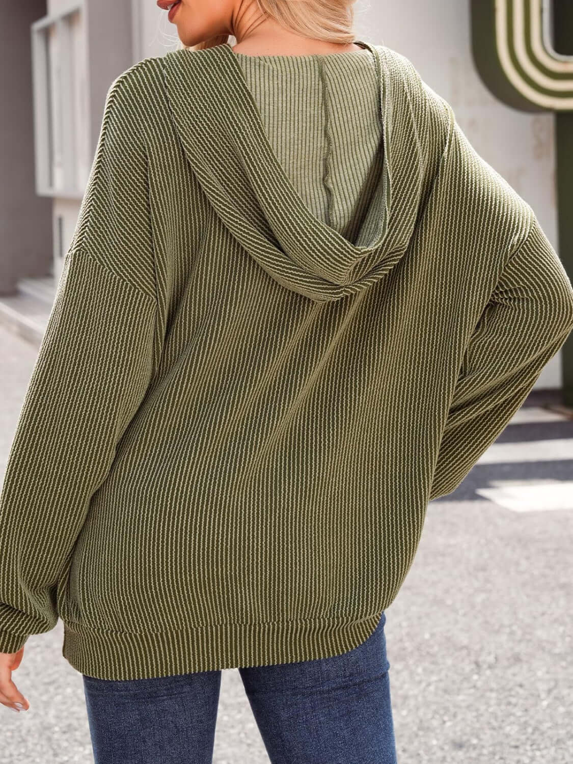 Textured kangaroo pocket long sleeve hoodie in olive green worn by model with back view, emphasizing ribbed fabric and hood.