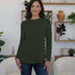 Woman wearing FAM-FAM army green round neck long sleeve t-shirt with decorative buttons, standing in a stylish modern room.