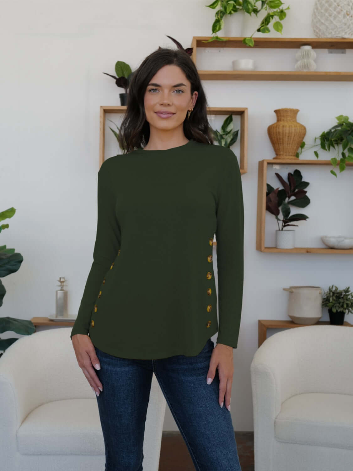 Woman wearing FAM-FAM army green round neck long sleeve t-shirt with decorative buttons, standing in a stylish modern room.