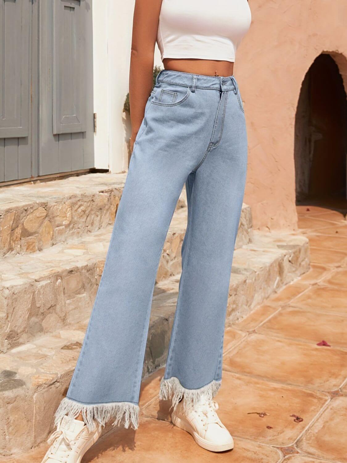 Woman in light wash bootcut jeans with raw hem and fringe, paired with a crop top, showcasing a stylish summer look.