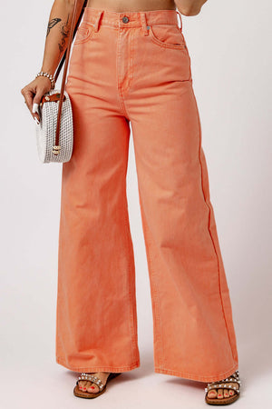 Bright orange wide leg high waist jeans styled with a white woven handbag and bejeweled sandals.