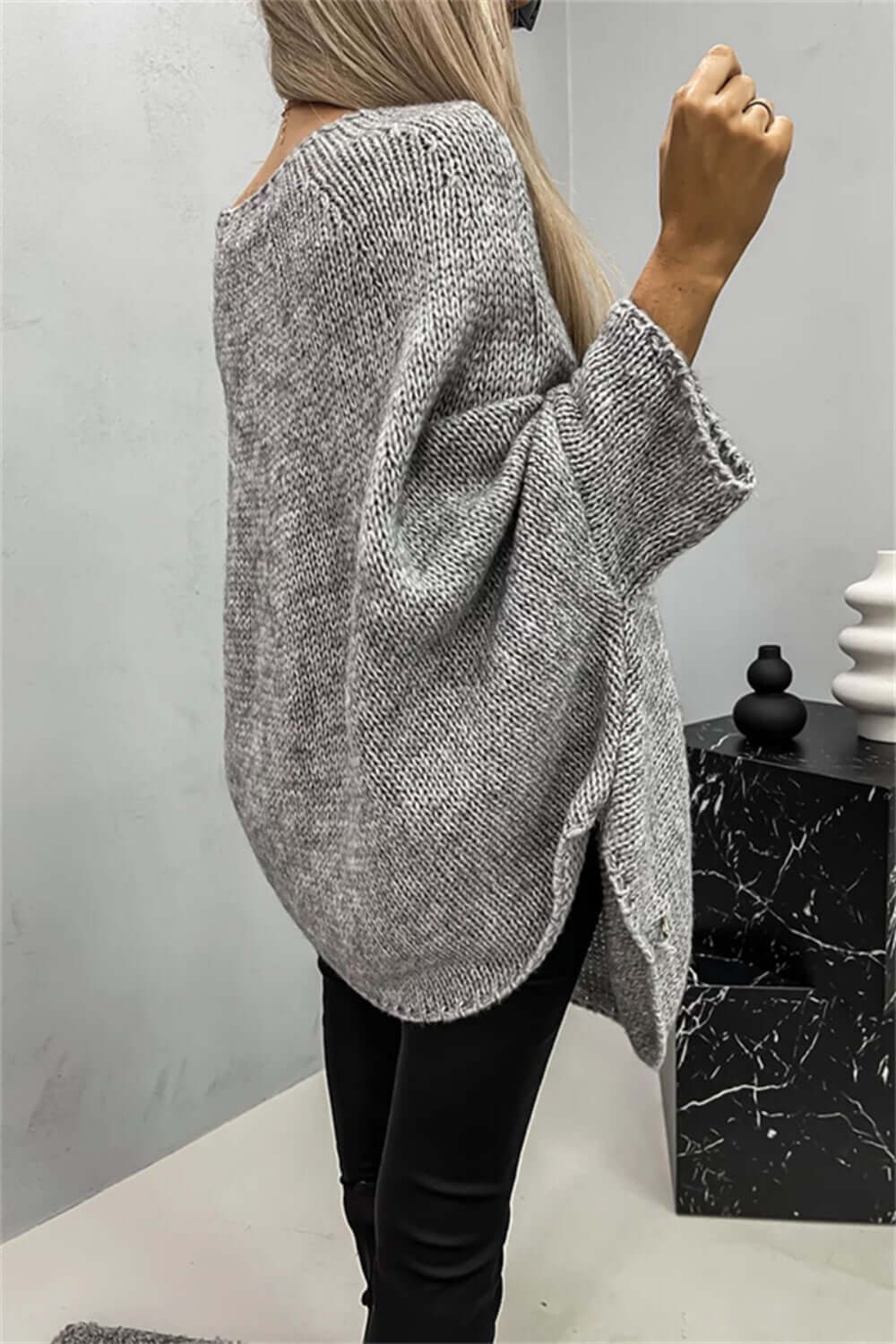 Cozy grey batwing sleeve sweater with a round neck, styled elegantly with black pants in a modern setting.