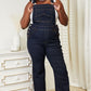 Woman wearing High Waist Classic Denim Overalls by Judy Blue Jeans, showcasing vintage charm with a modern twist in stylish home setting.