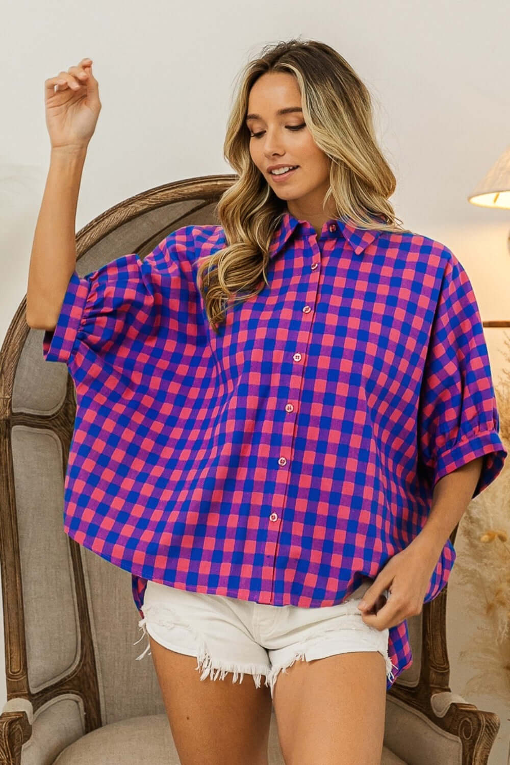 Woman wearing Plaid Button Up Dolman Sleeve Shirt with blue and pink checkered pattern and white shorts standing indoors