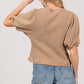 Back view of a model wearing a stylish tan puff-sleeve waffle knit top with denim shorts.