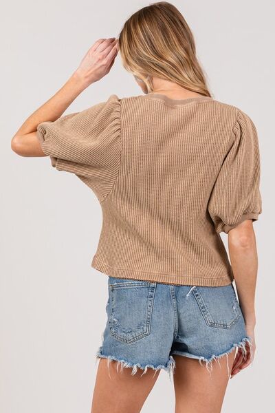 Back view of a model wearing a stylish tan puff-sleeve waffle knit top with denim shorts.