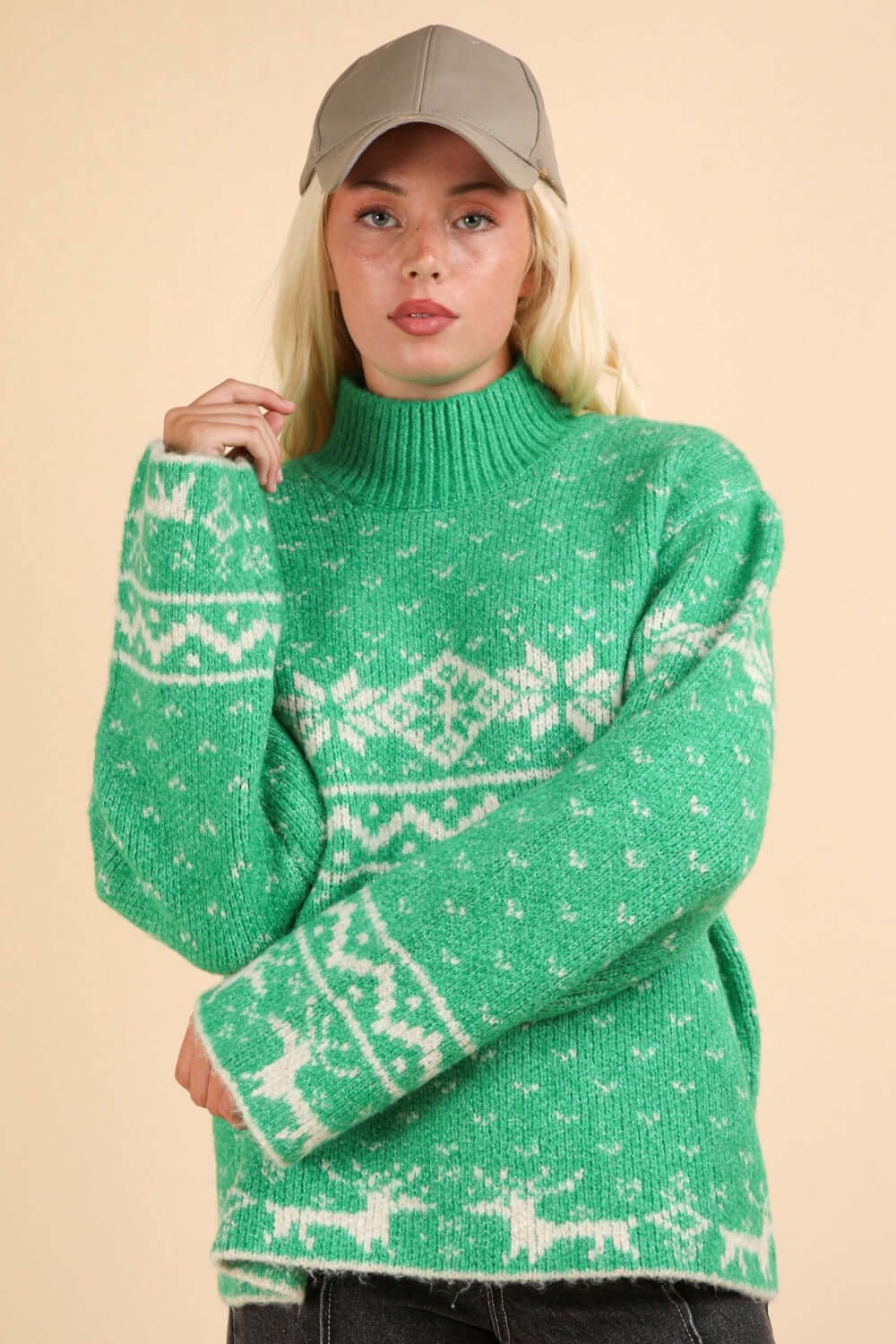 Woman wearing green Christmas sweater with snowflake and reindeer design, mock neck, and long sleeves, paired with a gray cap.