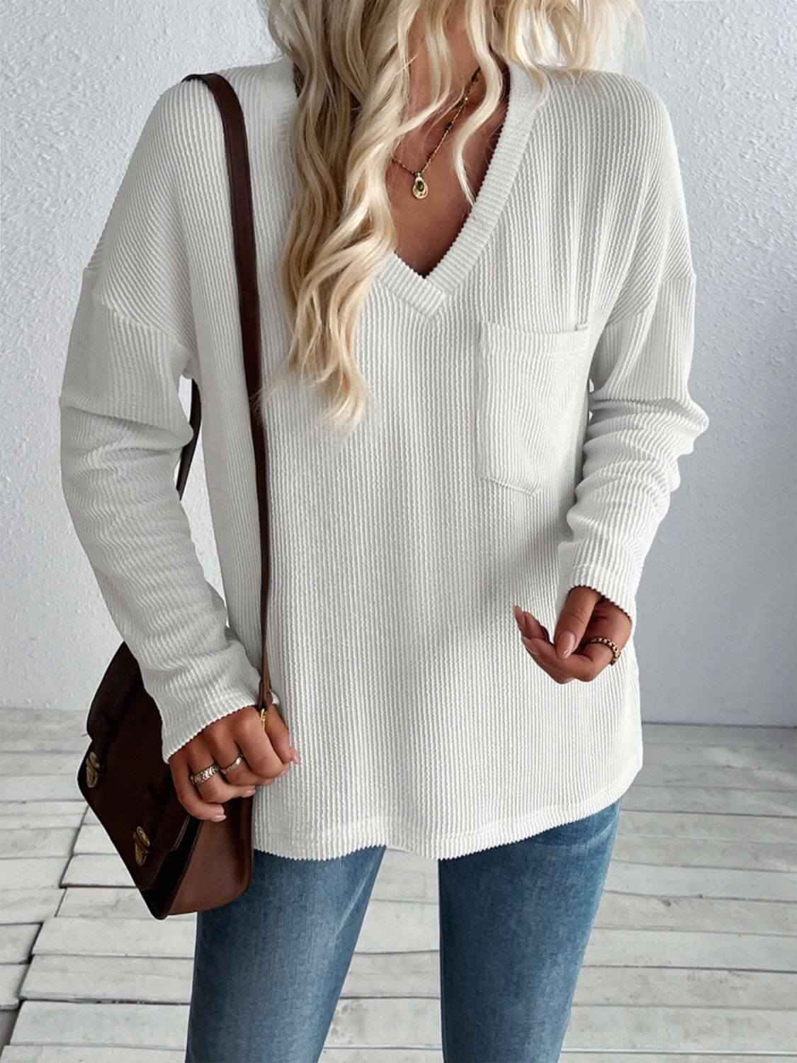 Woman wearing Double Take Pocketed Textured V-Neck Long Sleeve T-Shirt in white with jeans and a shoulder bag