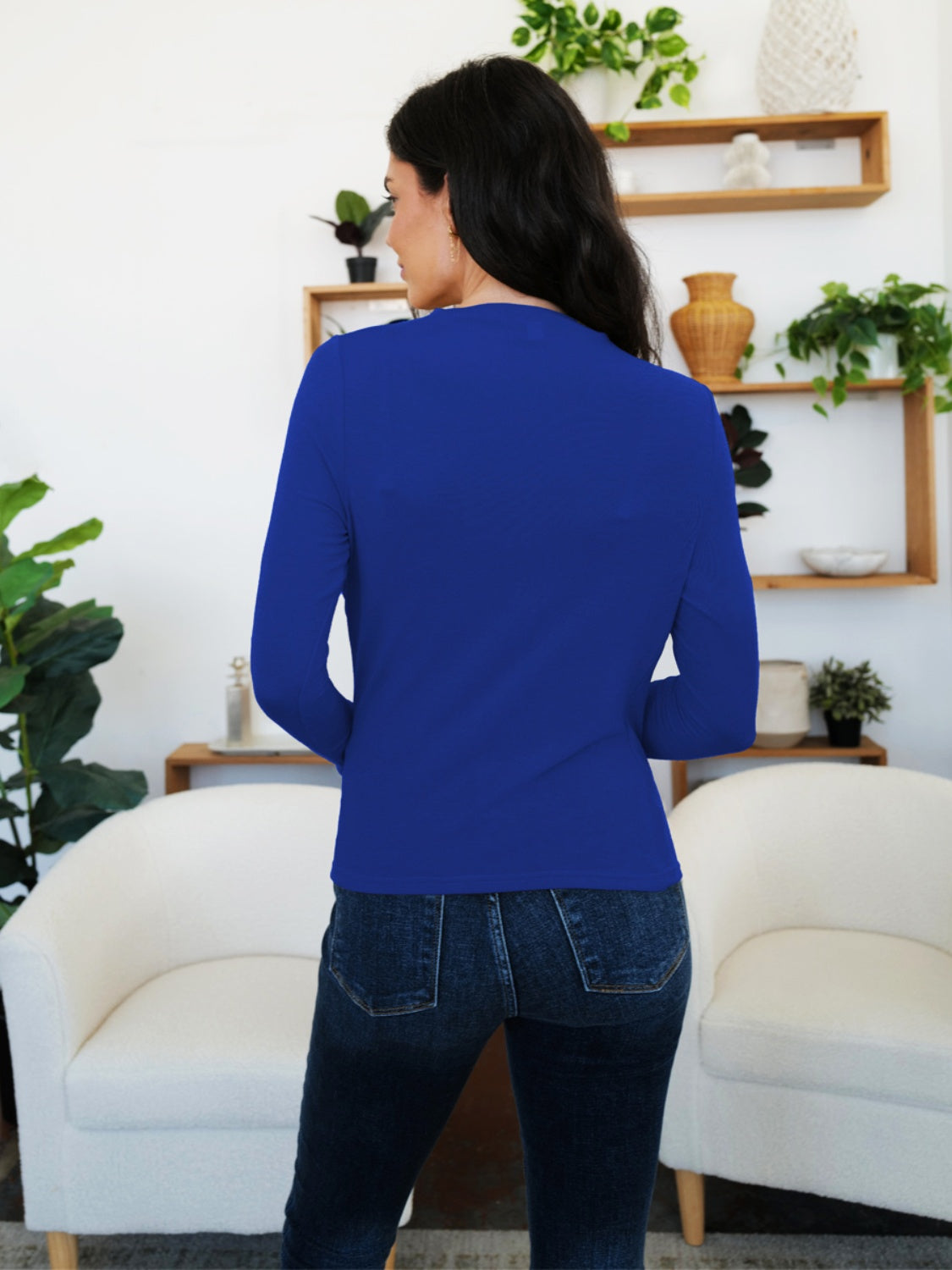 Woman in French Blue FAM-FAM Ruched Mock Neck Long Sleeve T-Shirt, styled with jeans, stands in a cozy room.