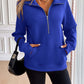 Woman wearing a blue Ivy Lane Half Zip Raglan Sleeve Sweatshirt with pockets, paired with black shorts and a black handbag.