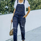 Woman wearing pocketed distressed denim overalls outdoors, styled casually with a white T-shirt and heels.