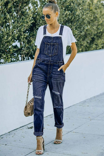 Woman wearing pocketed distressed denim overalls outdoors, styled casually with a white T-shirt and heels.