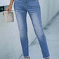 Woman wearing high waist raw hem skinny jeans with slight stretch and pockets, styled casually outdoors, holding a beige clutch.