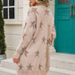 Woman in angel wings star cardigan with playful design stands stylishly outdoors in charming setting.