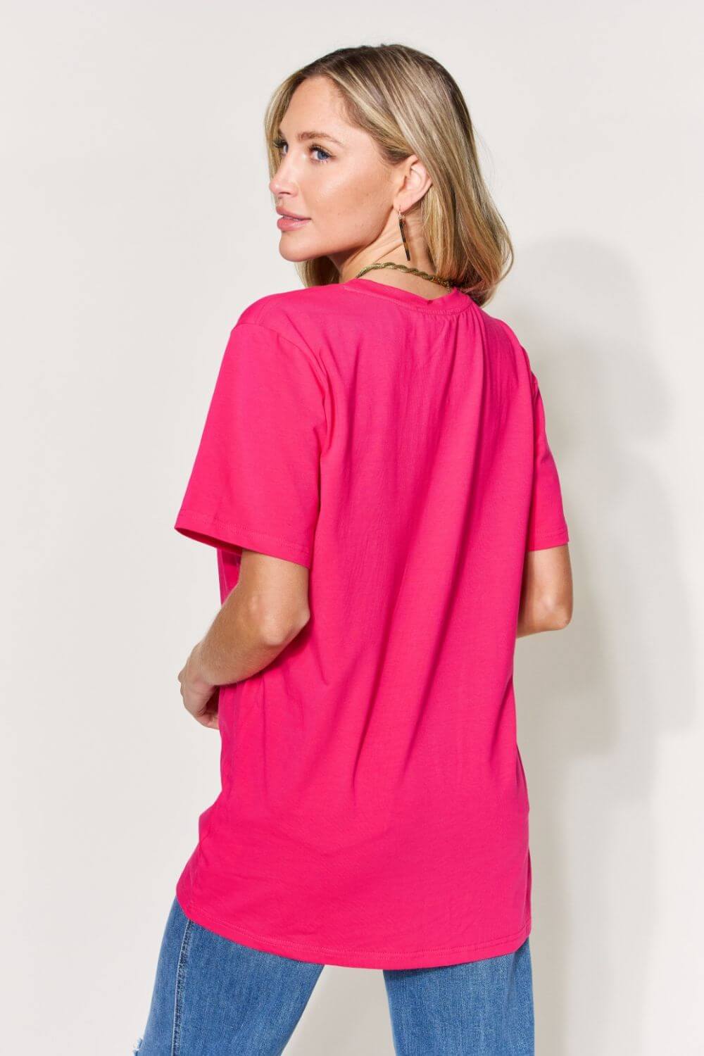 Woman wearing a vibrant pink graphic round neck short sleeve T-shirt, showcasing back view, paired with blue jeans.