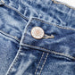 Close-up of distressed raw hem bootcut jeans waistband and button detail in blue denim.