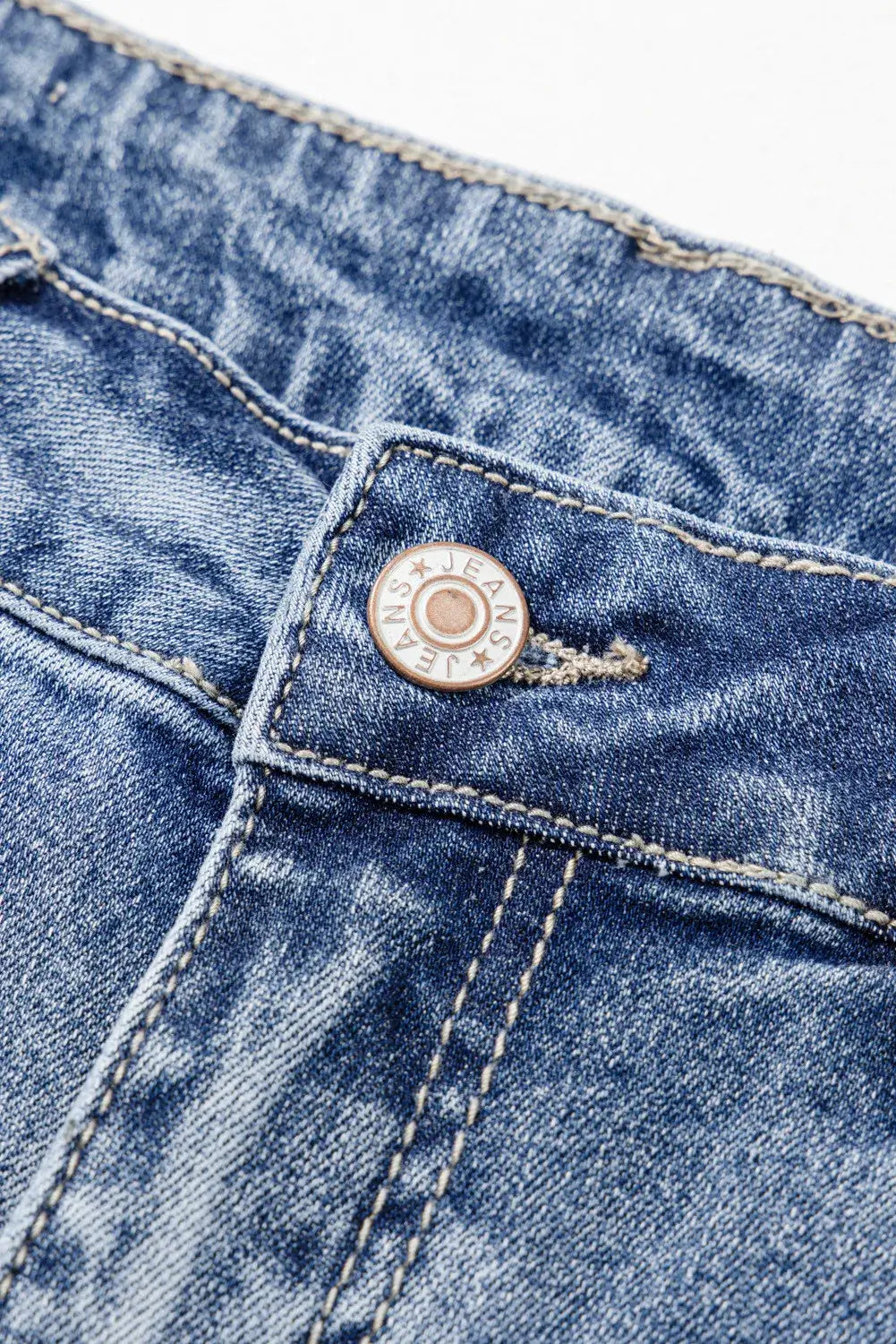 Close-up of distressed raw hem bootcut jeans waistband and button detail in blue denim.