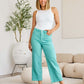 Woman wearing turquoise high-waisted raw hem jeans and white tank top in modern living room setting