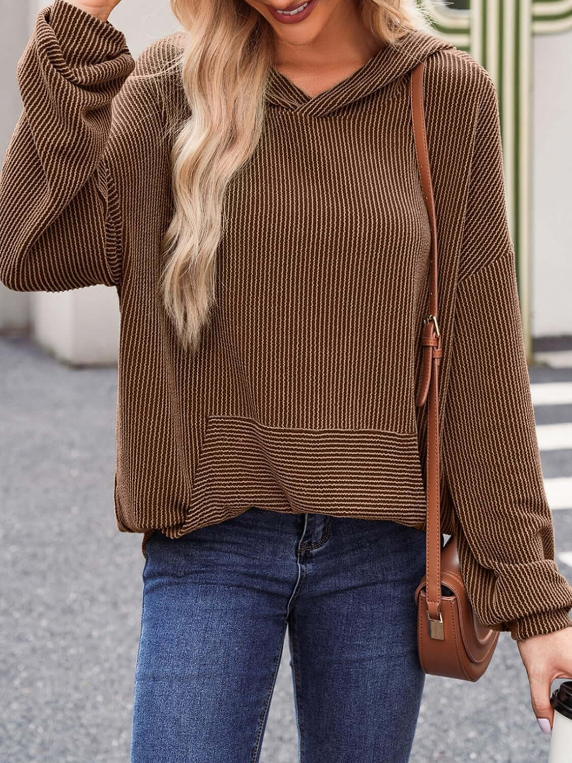 Woman wearing textured kangaroo pocket long sleeve hoodie with jeans and a brown shoulder bag.