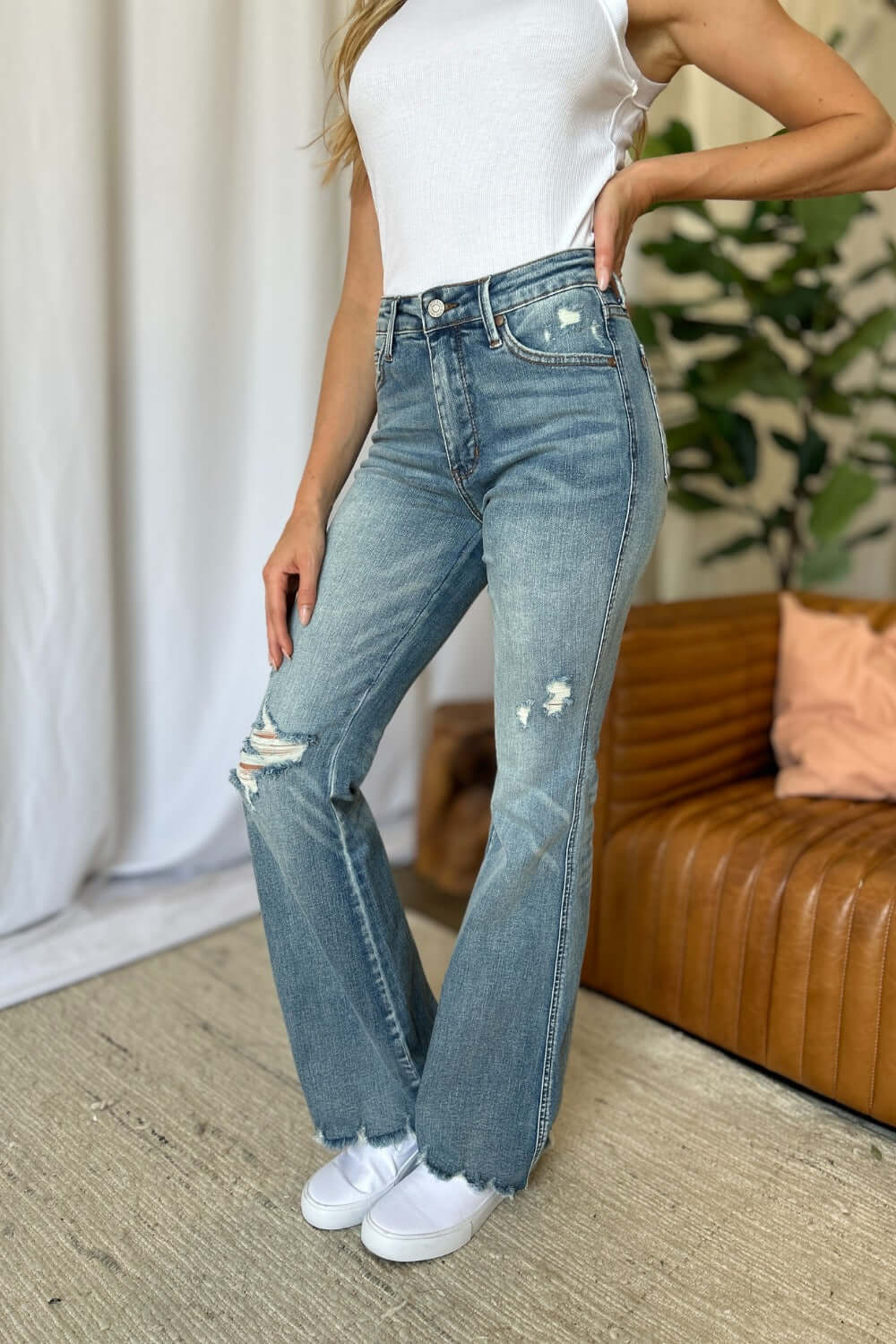 Woman wearing Judy Blue medium rise tummy control destroy flare jeans with distressed details and a white tank top.