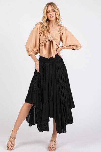 Stylish woman in a handkerchief hem black midi skirt and a beige blouse with a tie front, showcasing a chic outfit.