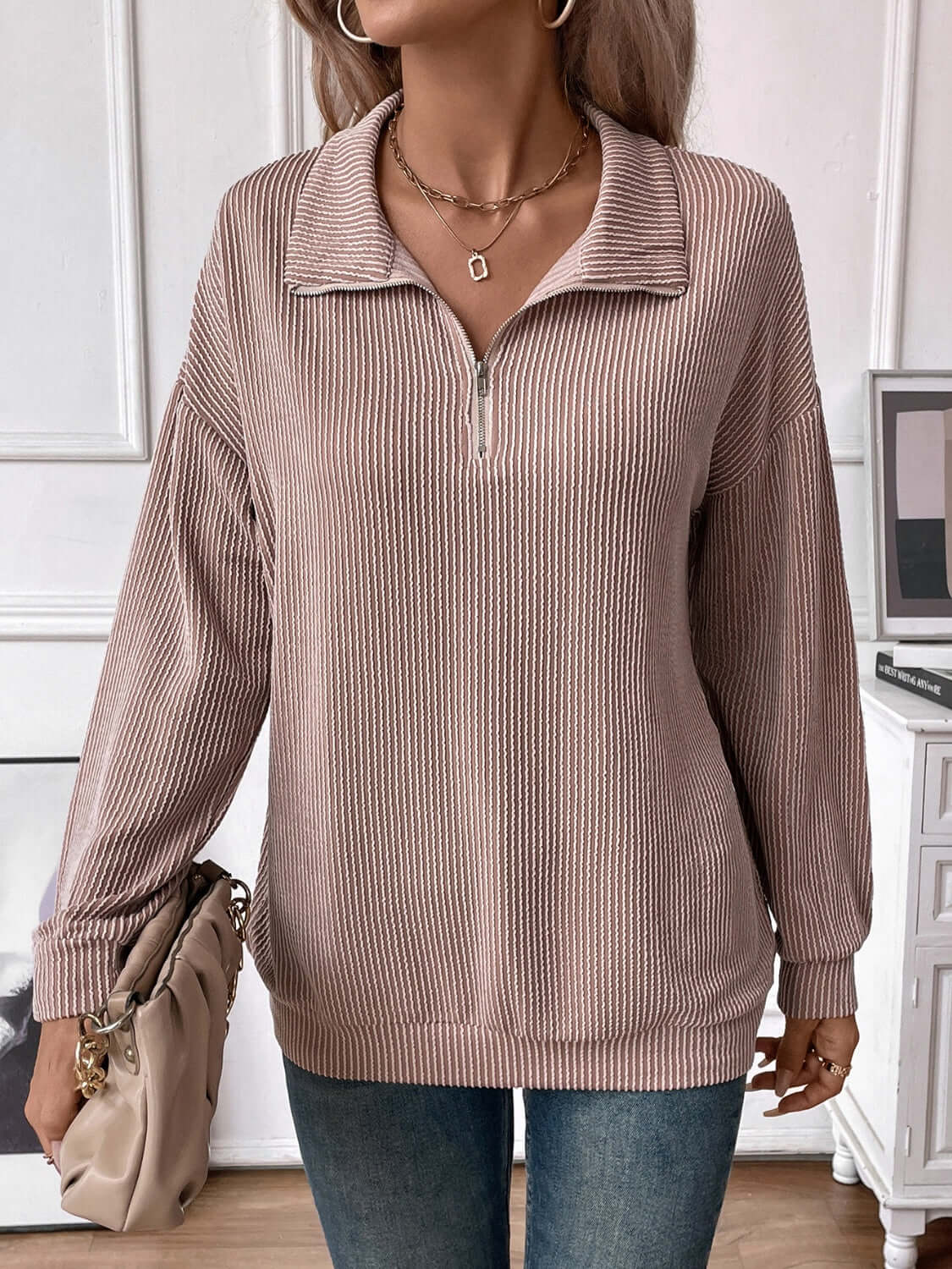 Woman wearing a Striped Half Zip Long Sleeve T-Shirt in beige with slightly stretchy material and accessorized with a necklace and handbag in a modern setting.