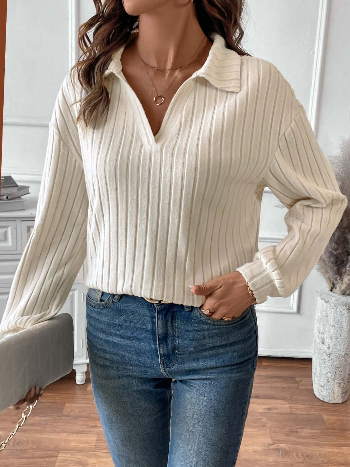 Woman wearing ribbed Johnny collar long sleeve t-shirt in white styled with blue jeans in a living room setting.