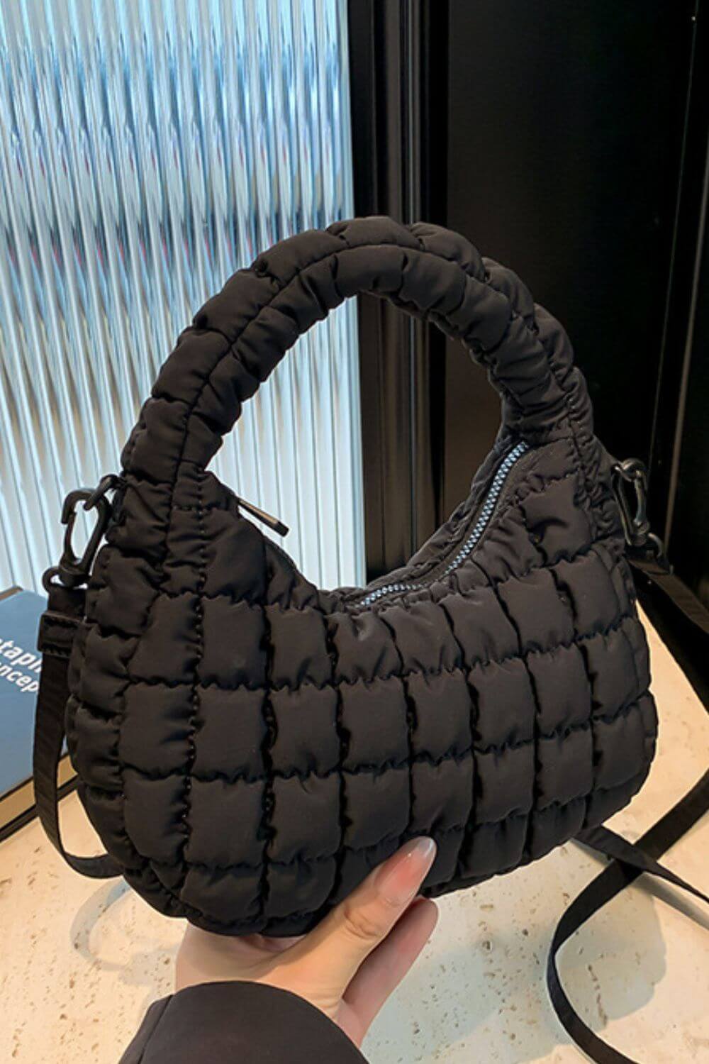 Black quilted puffy crossbody bag with removable strap, held in hand, showcasing stylish design and versatility for any occasion.