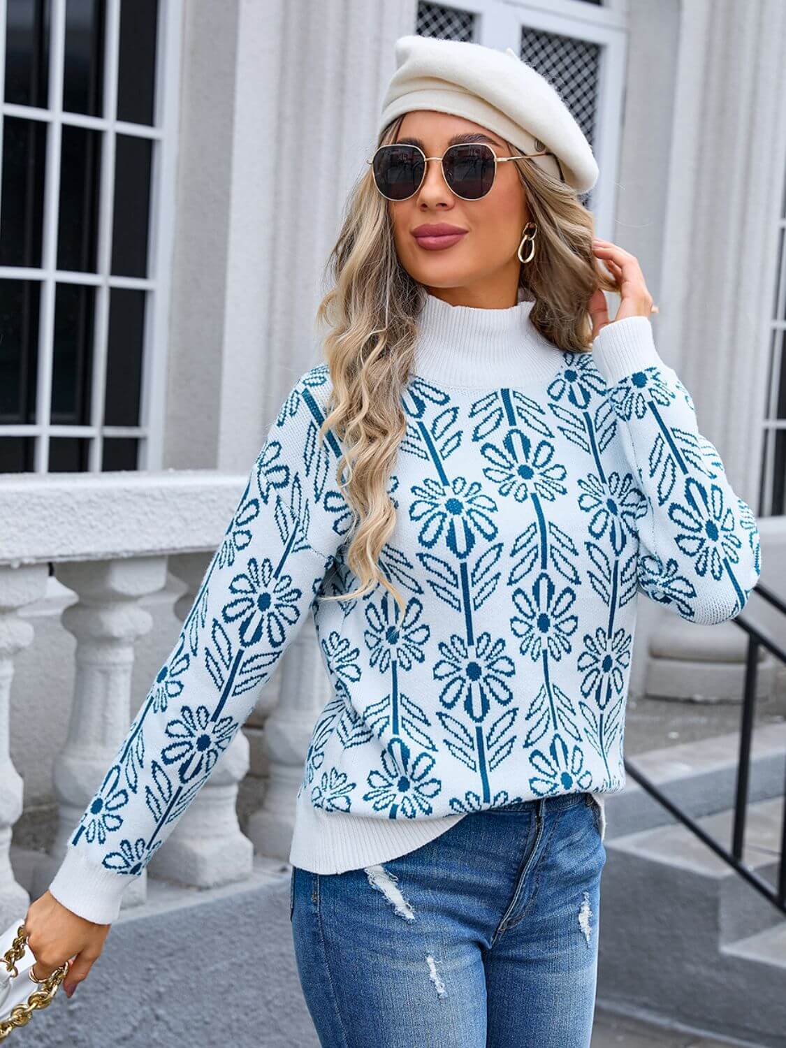 Woman in Angel Wings Flower Turtleneck Sweater with beret, standing stylishly outside in blue jeans and sunglasses.