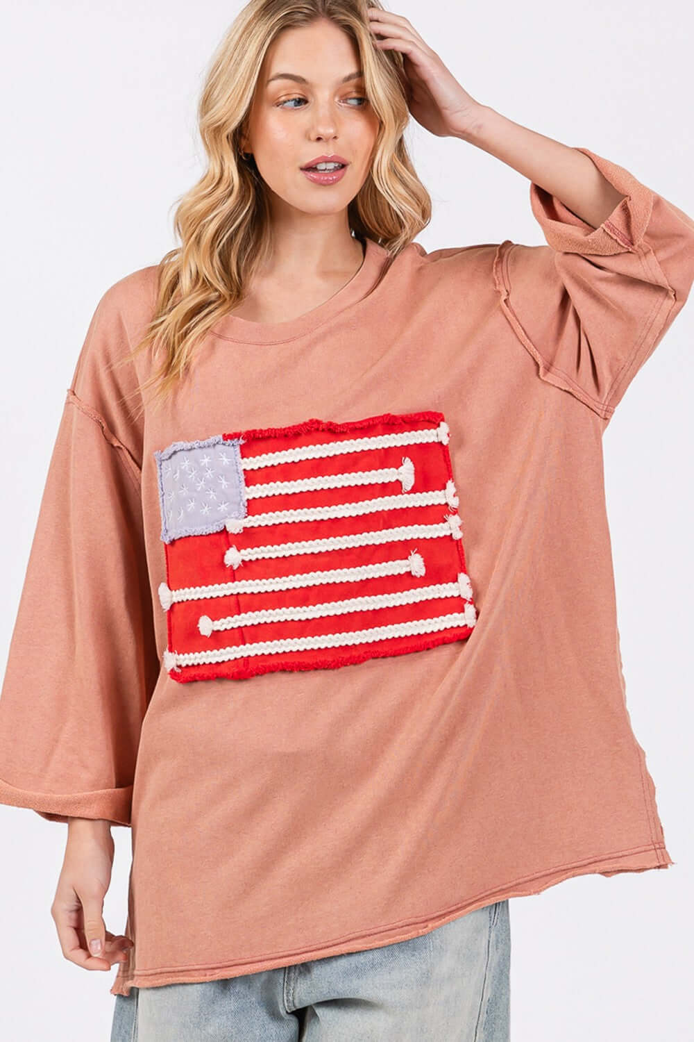 Woman wearing a full-size American Flag Patch Drop Shoulder T-Shirt with raw edge details and a relaxed fit, showcasing national pride.