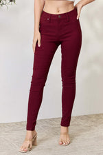 Woman wearing YMI Jeans Hyperstretch Mid-Rise Skinny Jeans in dark red, showcasing flexible and trendy design with faux front pockets.