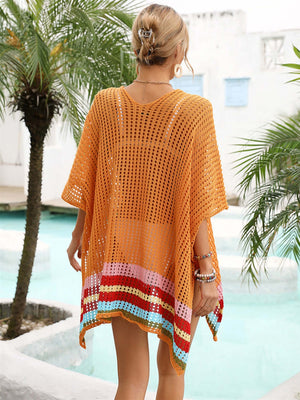 Woman wearing a slit openwork V-neck half sleeve cover-up in orange with colorful stripes, standing near a pool with palm trees in the background