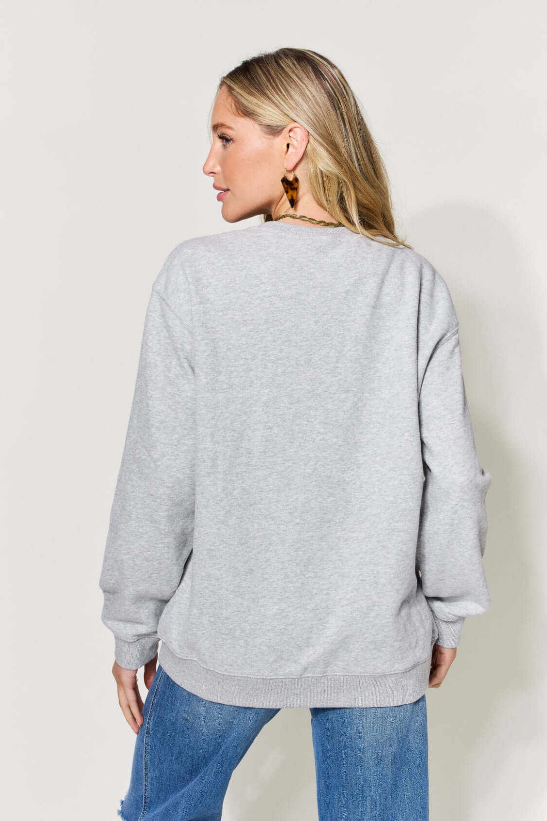 Woman wearing gray letter graphic long sleeve sweatshirt with blue jeans, shown from the back.