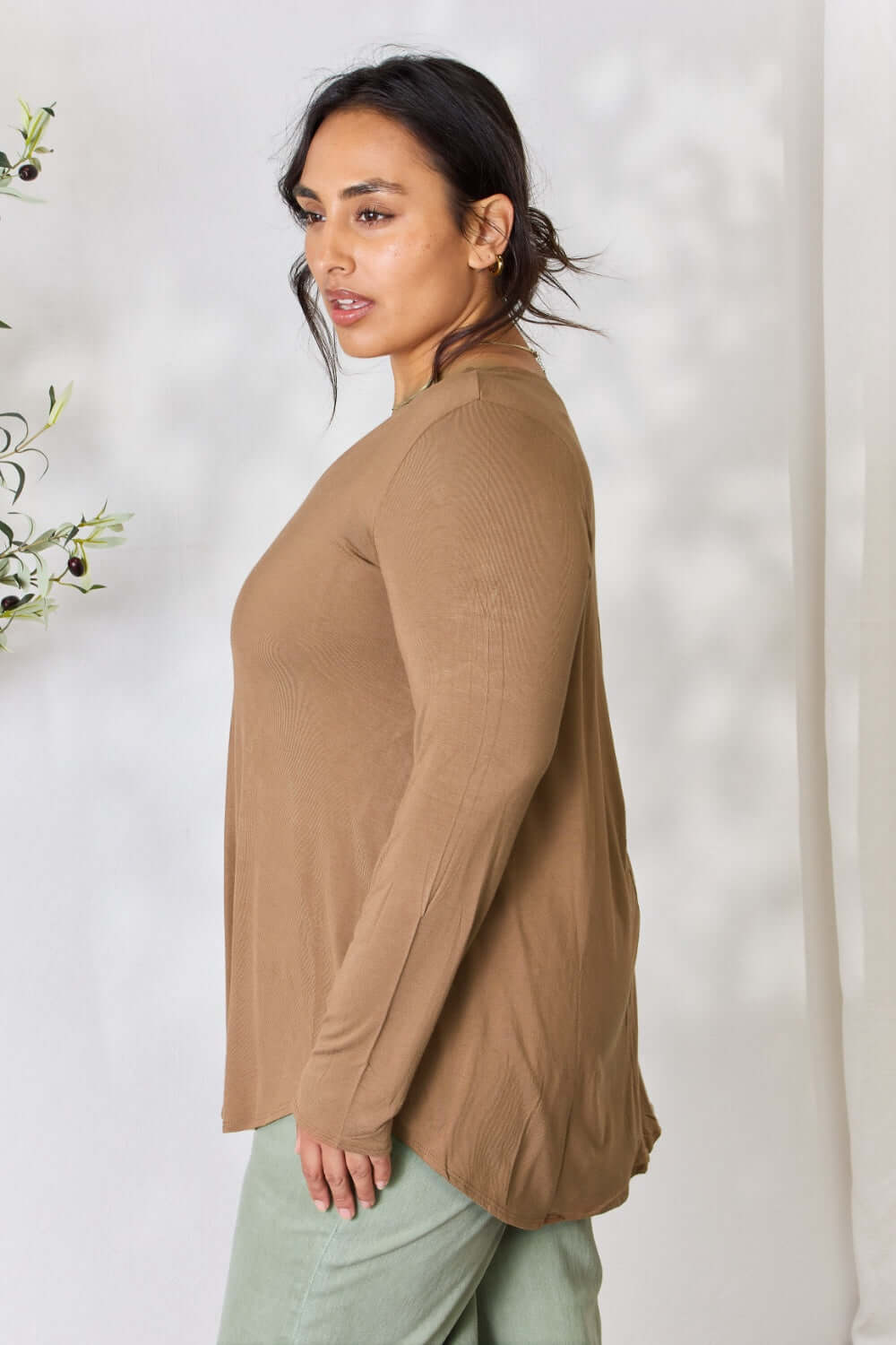 Woman wearing a long sleeve V-neck top in brown, paired with green pants, showcasing the side view of the outfit.