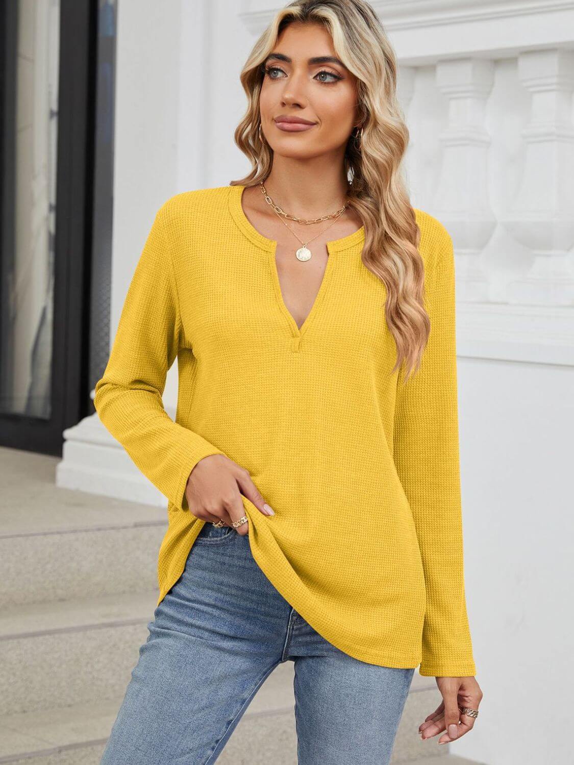 Woman wearing Bella Road Waffle-Knit Notched Long Sleeve T-Shirt in yellow, paired with blue jeans, standing on steps.