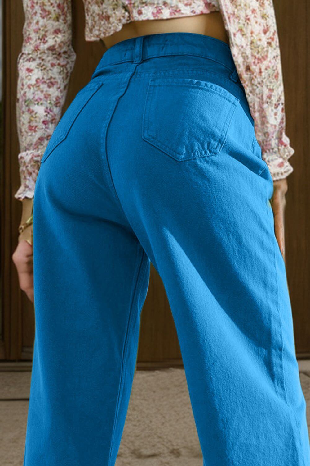 Woman wearing bright blue wide leg jeans with pockets, back view, paired with a floral crop top.