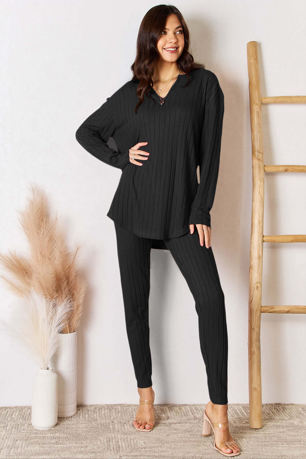 Woman wearing a notched long sleeve top and pants set in black, ribbed, slightly stretchy, polyester and elastane, fashionably styled indoor.