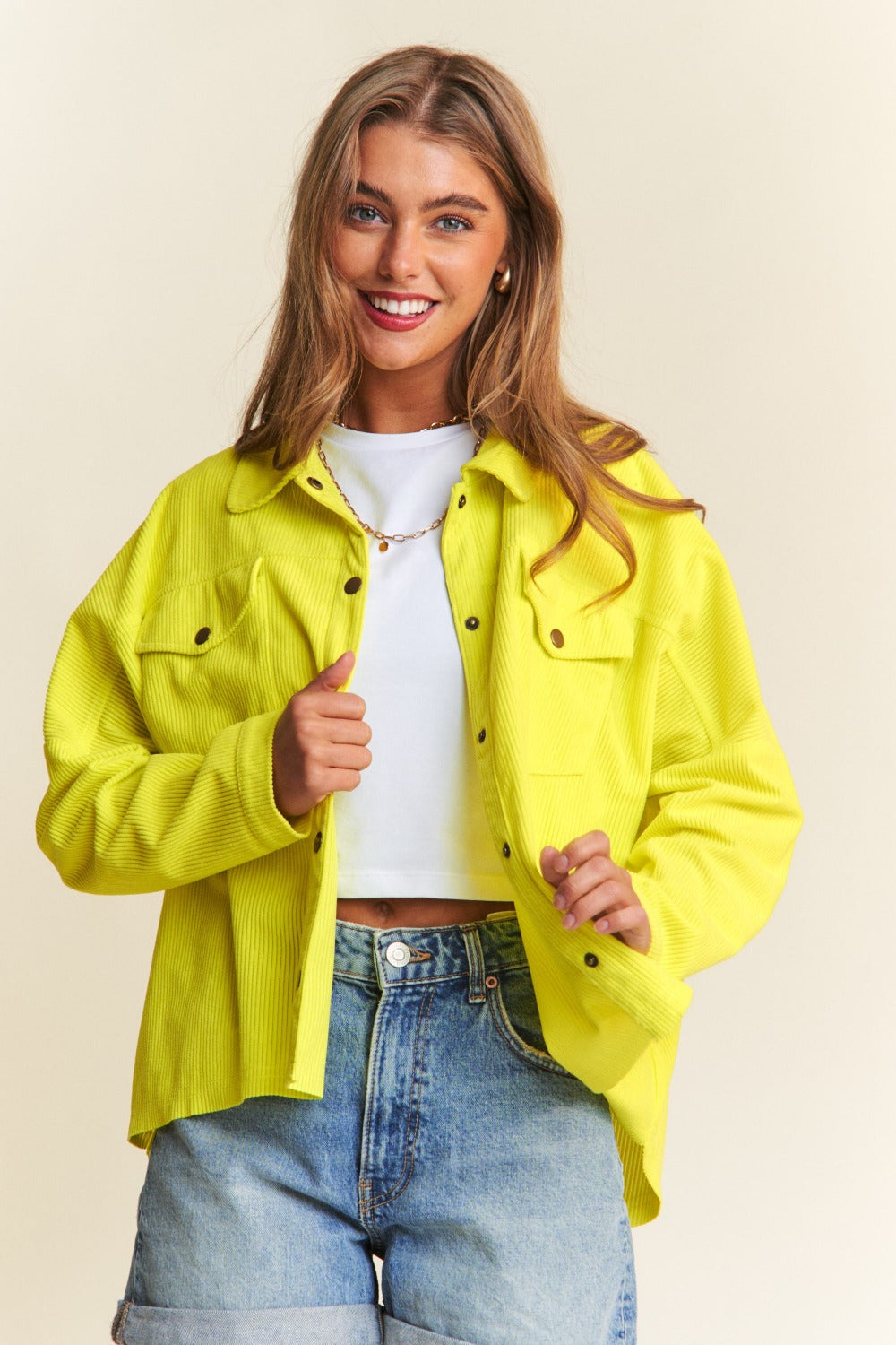 Woman wearing J.NNA snap down high low shacket in bright yellow, pairing it with a white top and blue jeans for a stylish look.