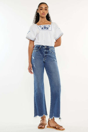 Woman wearing Kancan full-size high-rise slim wide-leg jeans with a white blouse, showcasing medium wash denim and unique hem details.