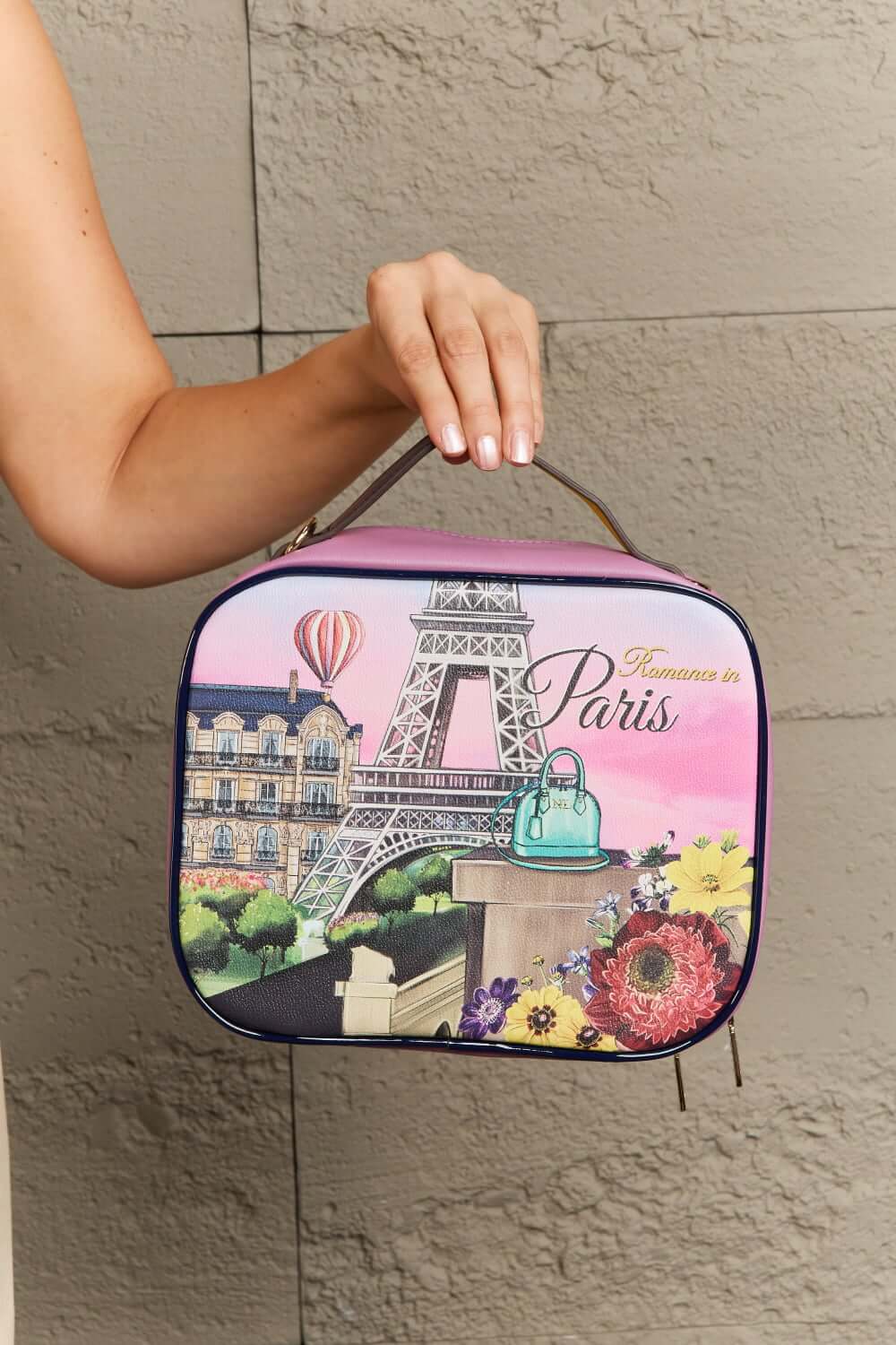 Hand holding a Nicole Lee USA printed handbag with a Paris Eiffel Tower design, featuring vibrant colors and floral details