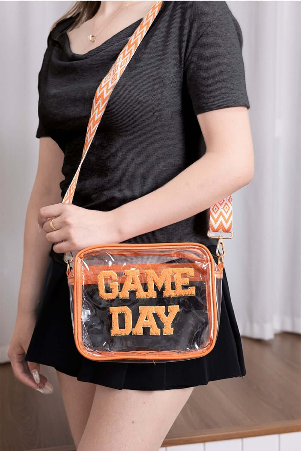 Woman holding a Zenana GAME DAY Transparent Crossbody Bag with glittered trim and adjustable strap, perfect for stadium use.