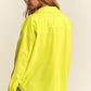 Woman wearing a yellow snap down long sleeve high low shacket with relaxed fit, paired with denim shorts, showcasing back view.