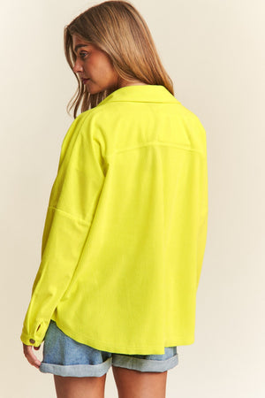 Woman wearing a yellow snap down long sleeve high low shacket with relaxed fit, paired with denim shorts, showcasing back view.